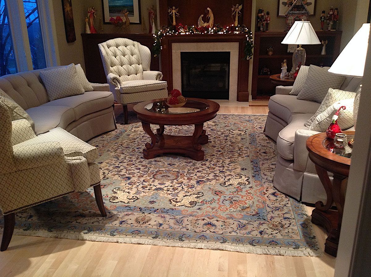 Cozy living room with light-colored furniture around a patterned rug and dark wood coffee table. Fireplace in background.