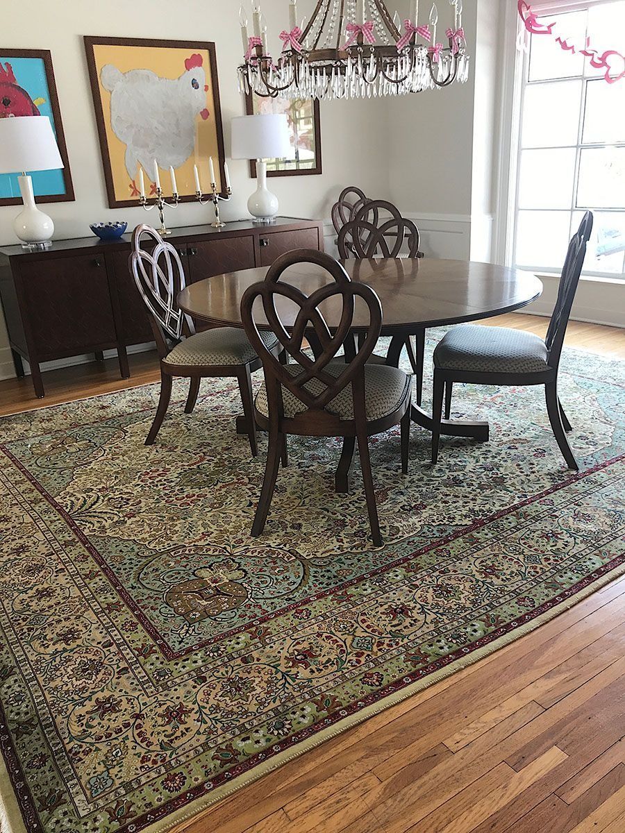 Dining room with round table, chairs, rug, and buffet. Artwork and chandelier in the background.