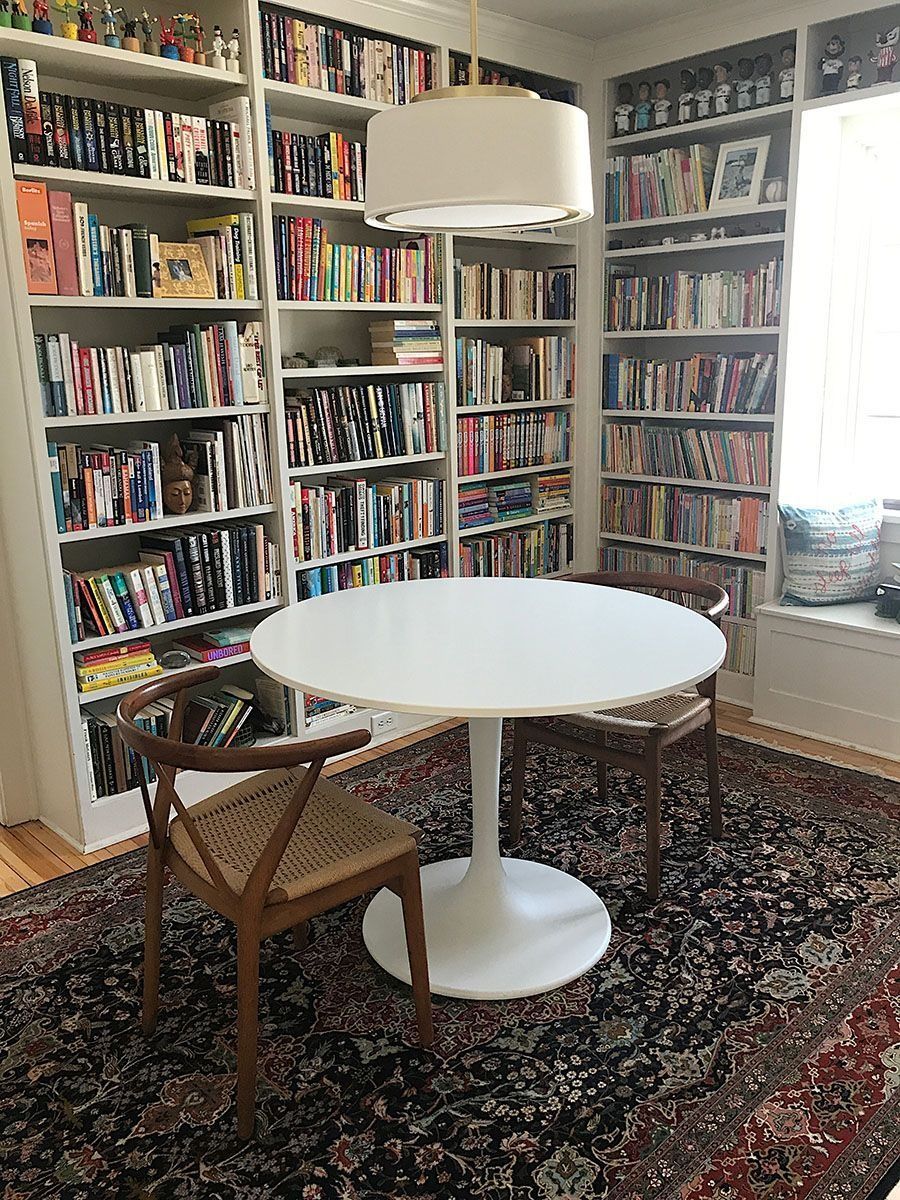 A cozy reading nook with bookshelves, a round white table, two chairs, and a rug.