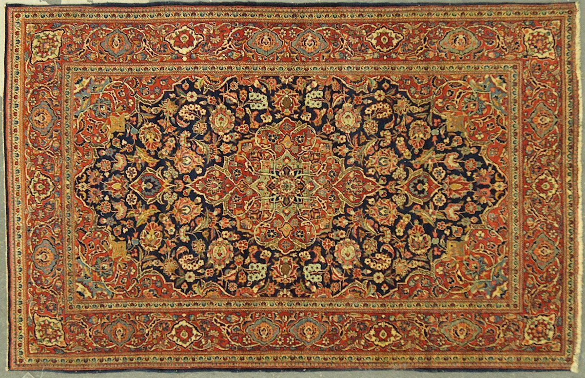 An ornate, rectangular Persian rug with a navy central medallion surrounded by floral designs in red and gold.