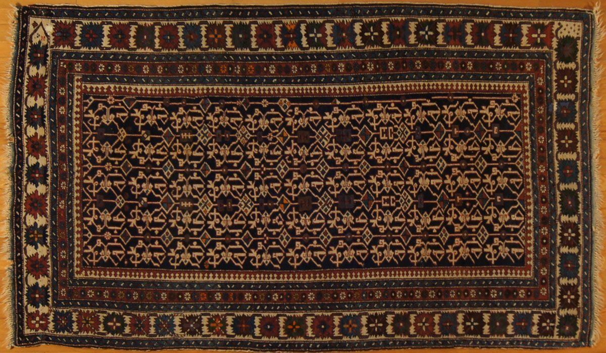 Dark blue and maroon patterned rug with fringe on a wood floor.