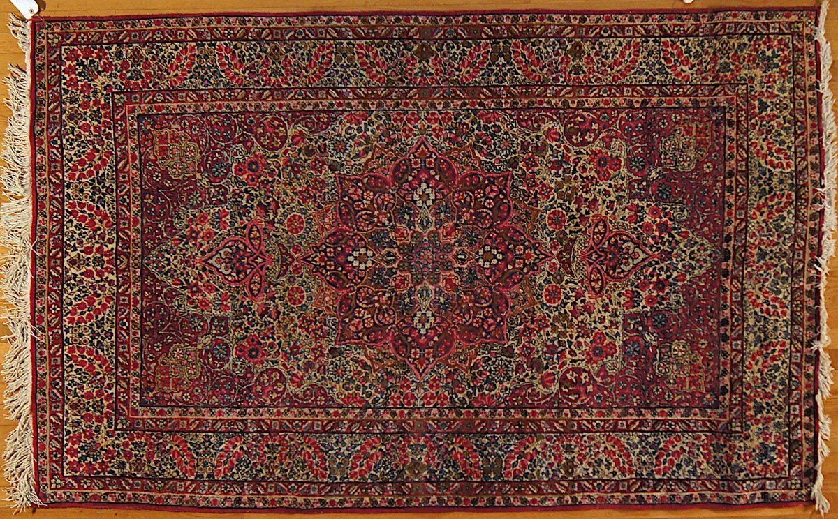 Red and dark green oriental rug with floral pattern and fringe.