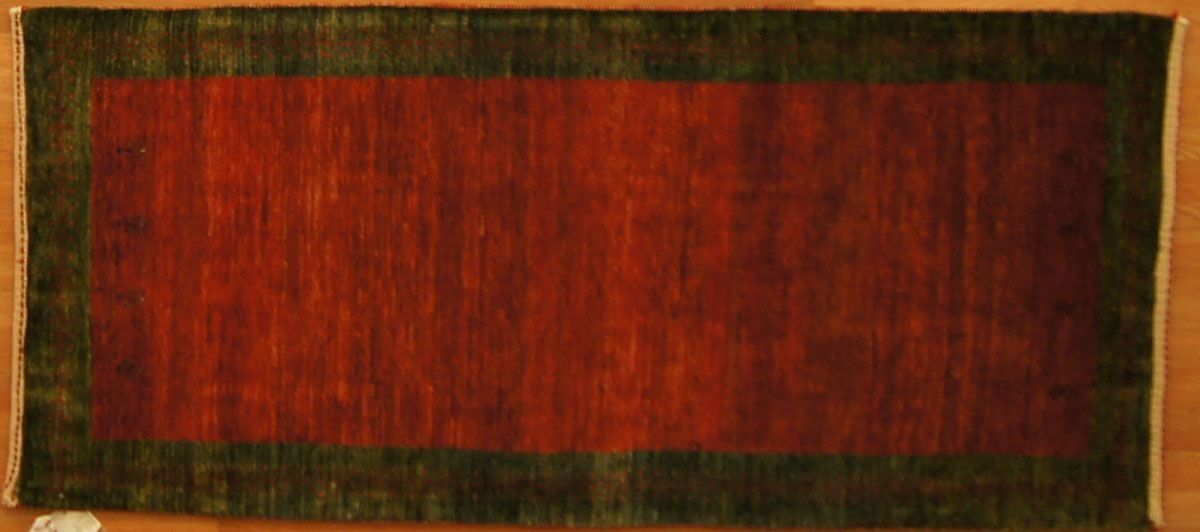 Red rug with a dark green border on a wooden floor.