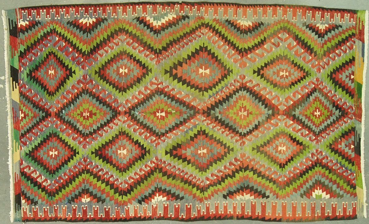 Geometric patterned rug with zig-zagging diamond shapes in green, red, and brown.
