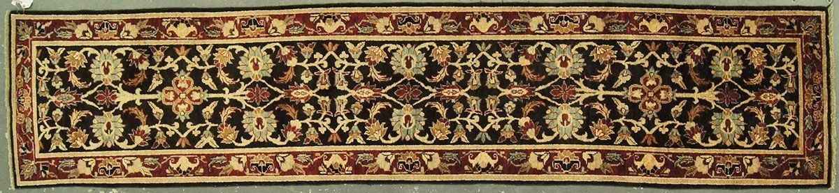 A narrow, rectangular rug with a dark field and floral designs bordered by a brown design.