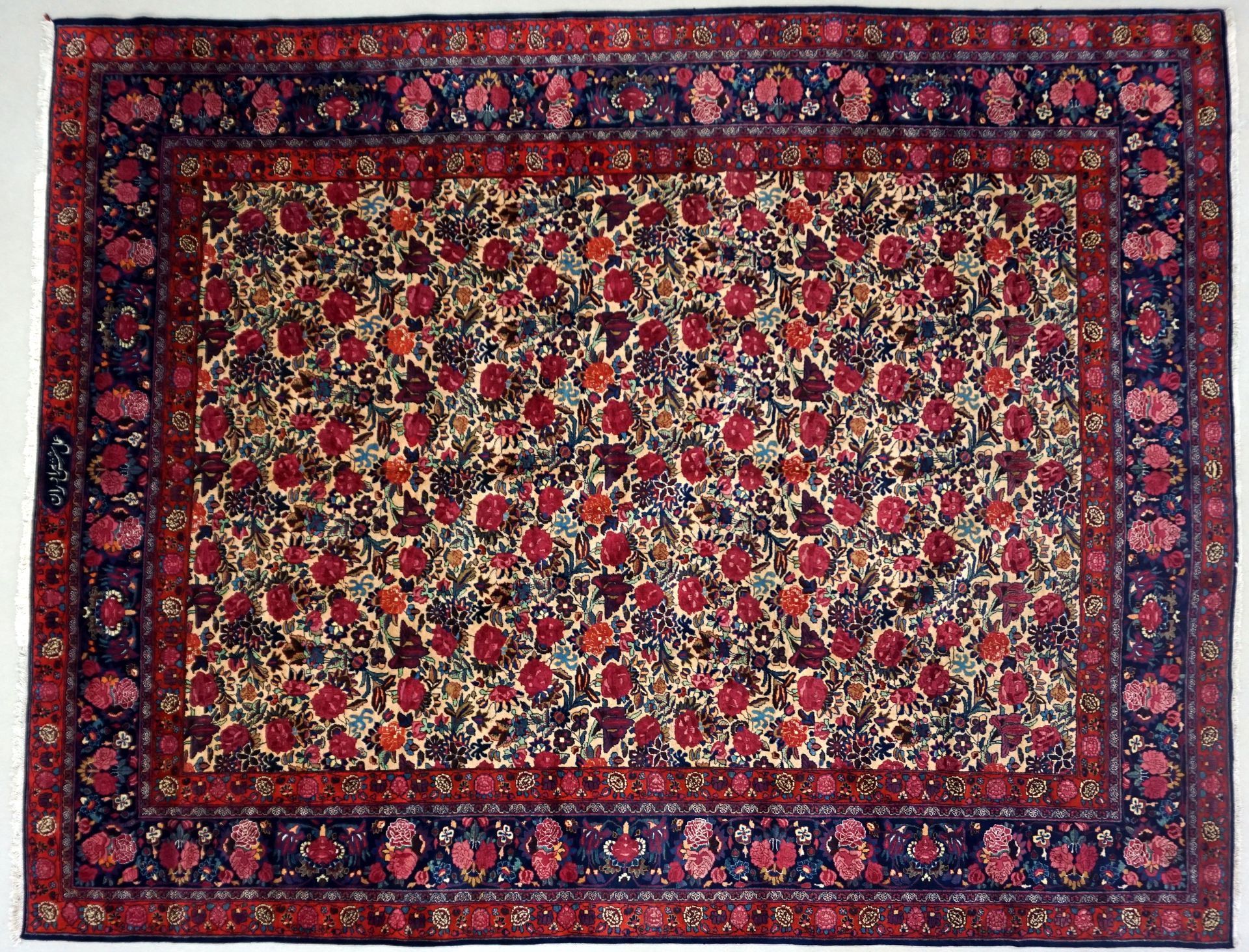 Persian rug with red floral pattern on cream field, framed by dark blue borders with floral and geometric designs.