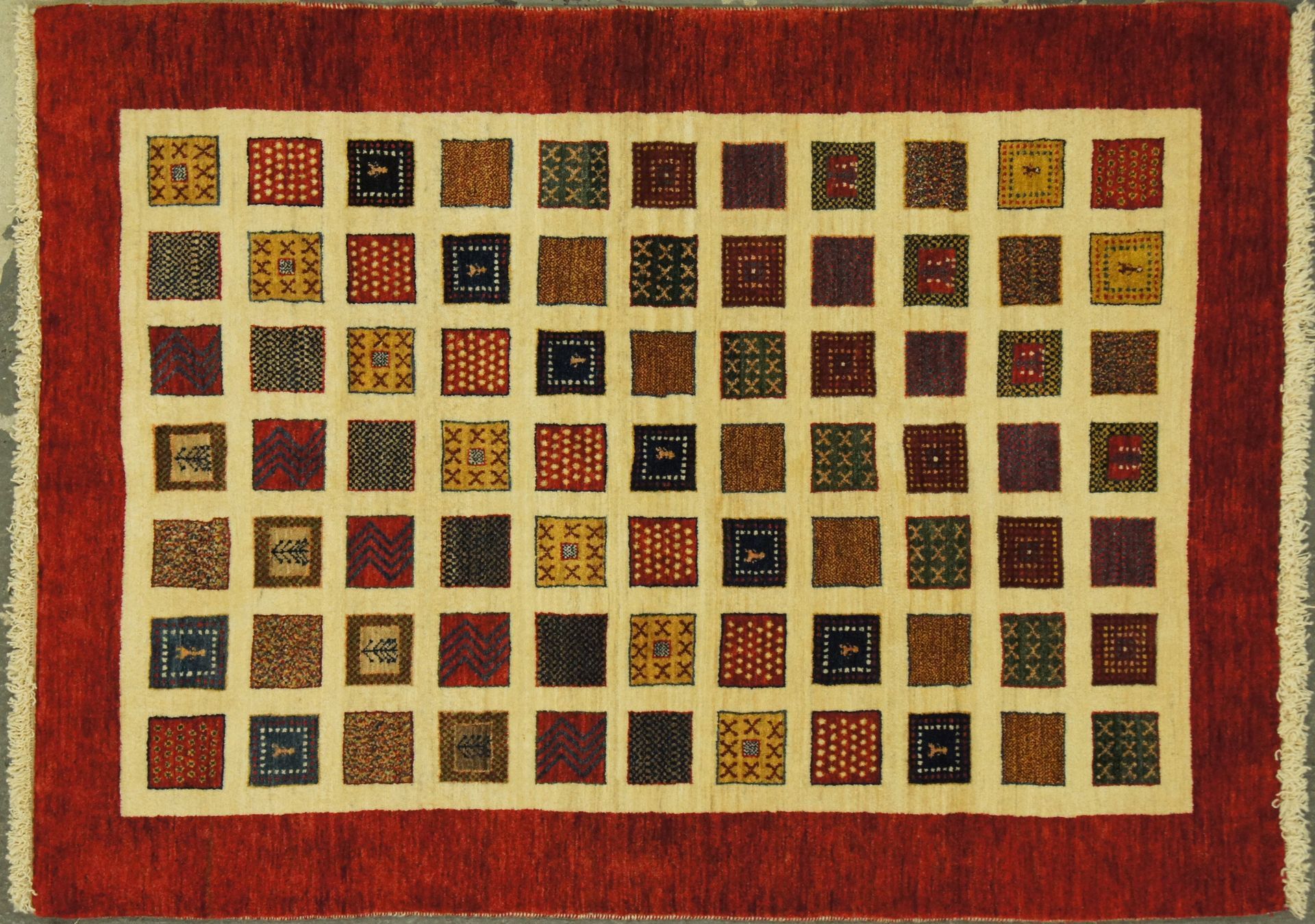 Red rug with cream-colored center, patterned with small squares in various colors.