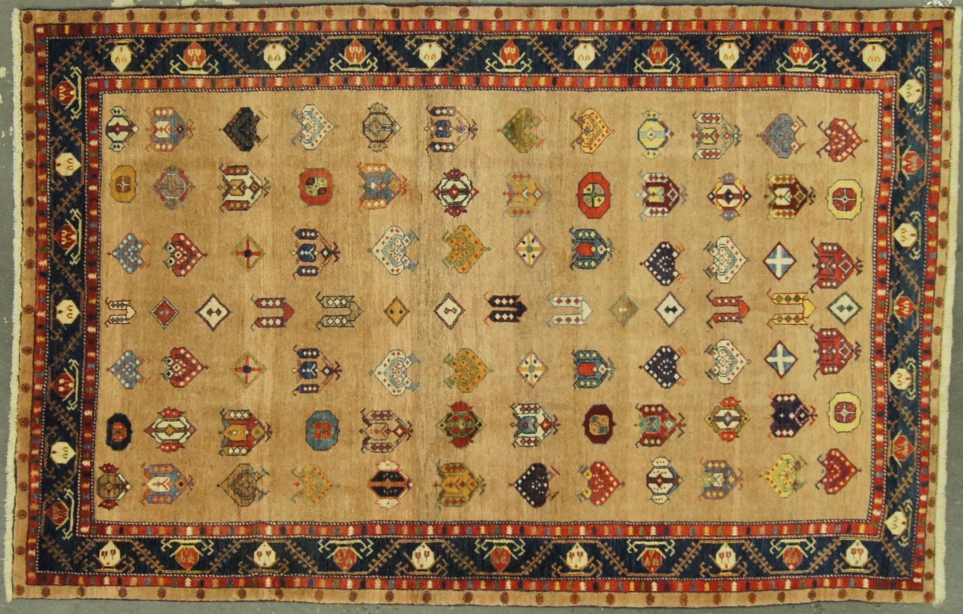 Rug with repeated geometric shapes in beige, red, blue, and brown, with a dark blue border.