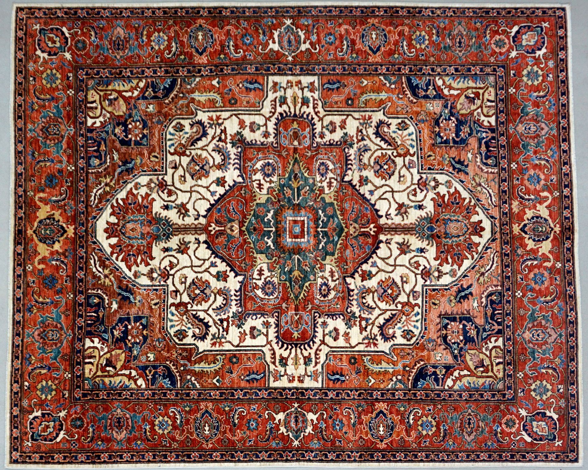 Ornate rectangular rug with a central medallion and detailed floral patterns in red, cream, and blue.