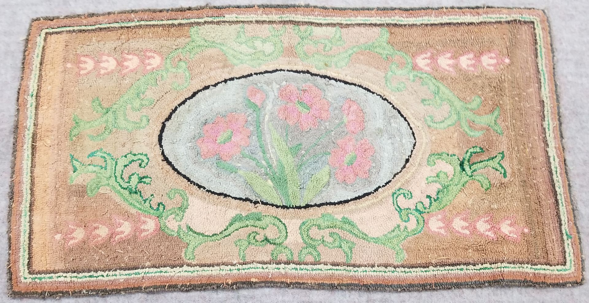 Hook rug with oval floral design in pink and green on a tan background