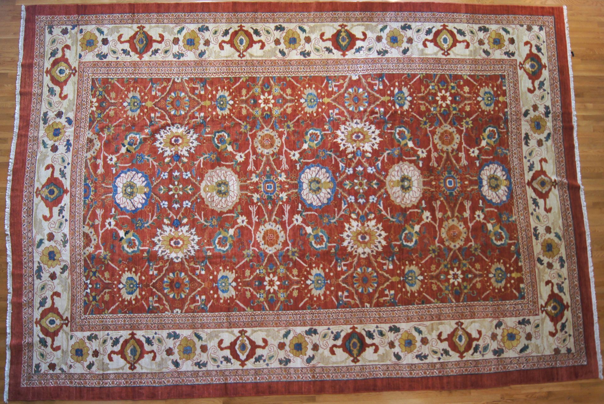 Red and cream Oriental rug with floral and geometric patterns on a wooden floor.