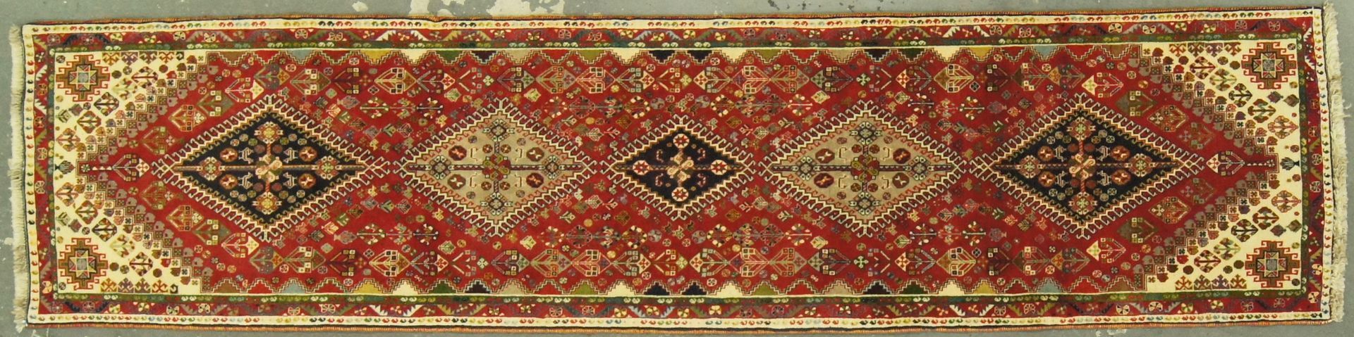 Rectangular rug with a red center, cream border, and diamond-shaped pattern.