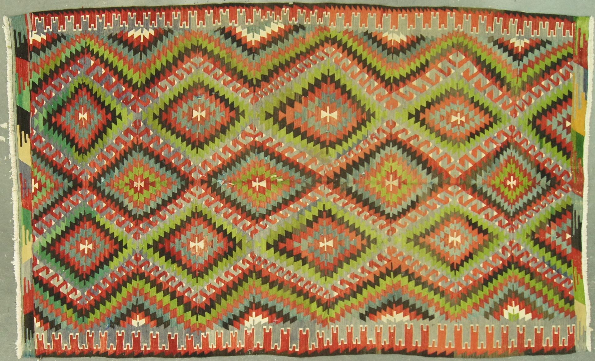 Colorful woven rug with diamond and zigzag patterns in greens, reds, and grays.