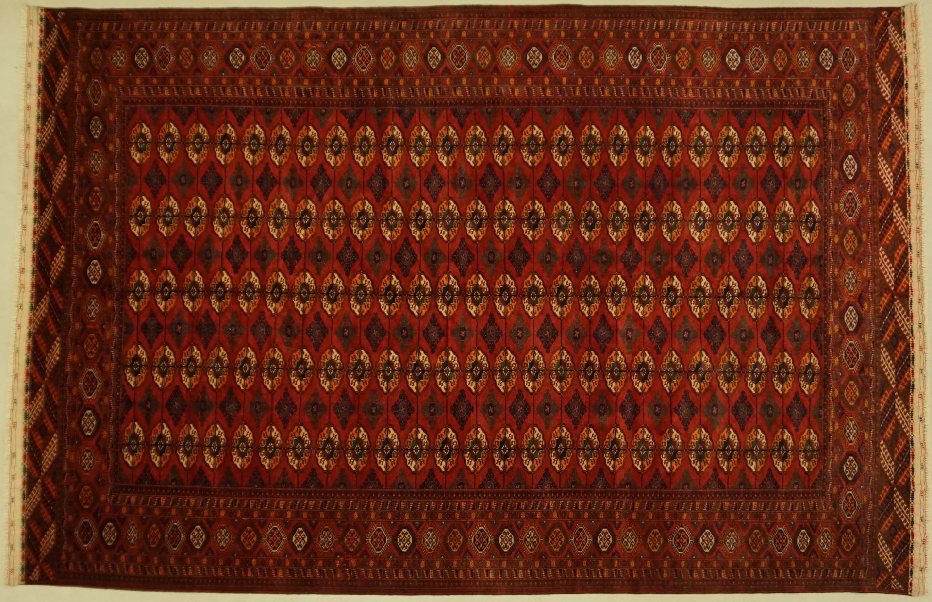 Red, rectangular Oriental rug with repeated diamond and floral patterns.