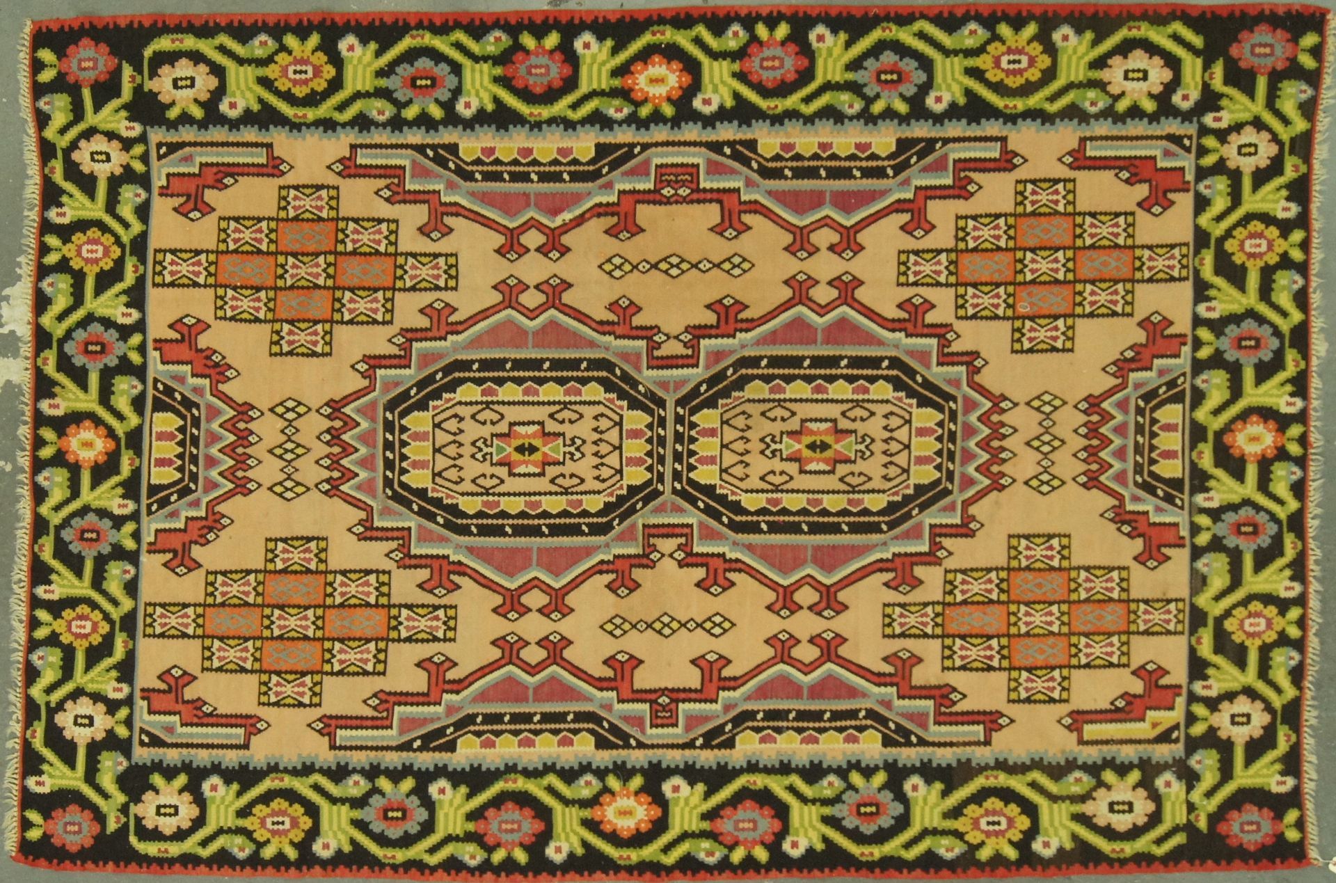 Tan, red, and black patterned rug with floral border.