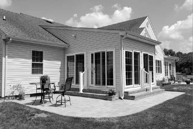 A black and white photo of a house with a patio in front of it.