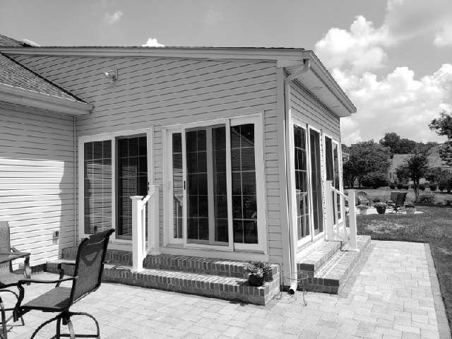 A black and white photo of a house with a patio and chairs.
