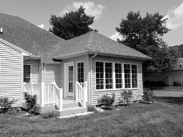 A black and white photo of a house with a screened in porch.