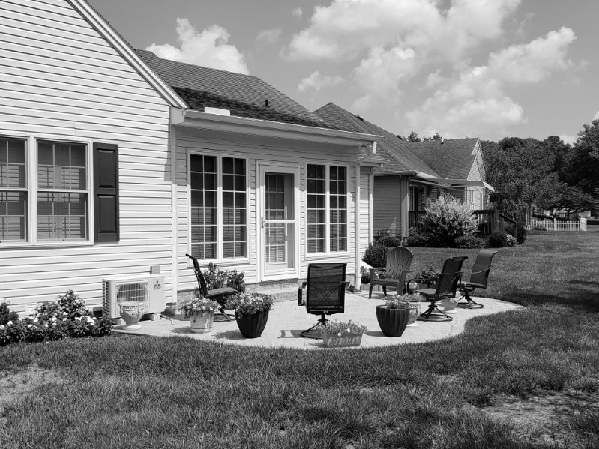 A black and white photo of a house with a patio in front of it.