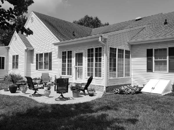 A black and white photo of a house with a patio in front of it