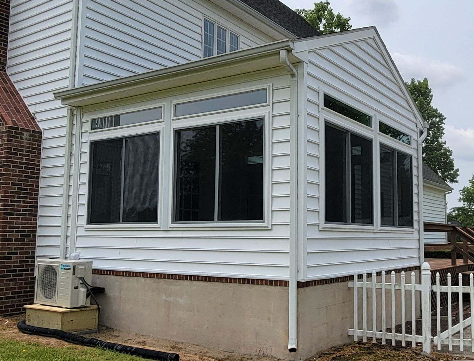 A white house with a screened in porch and a white fence.