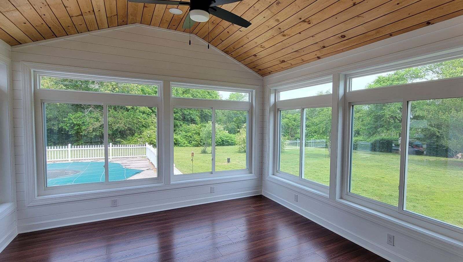 An empty room with a lot of windows and a ceiling fan.