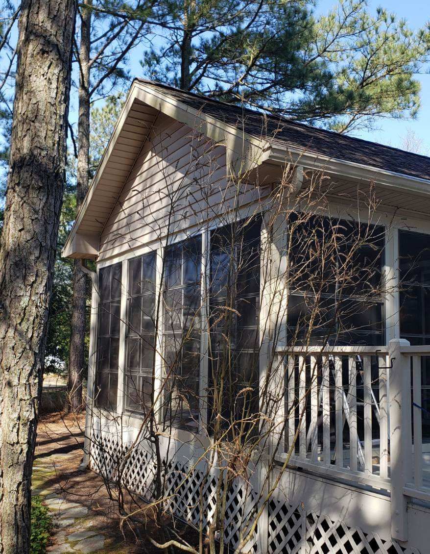 A small white house with a screened in porch and trees in the background .