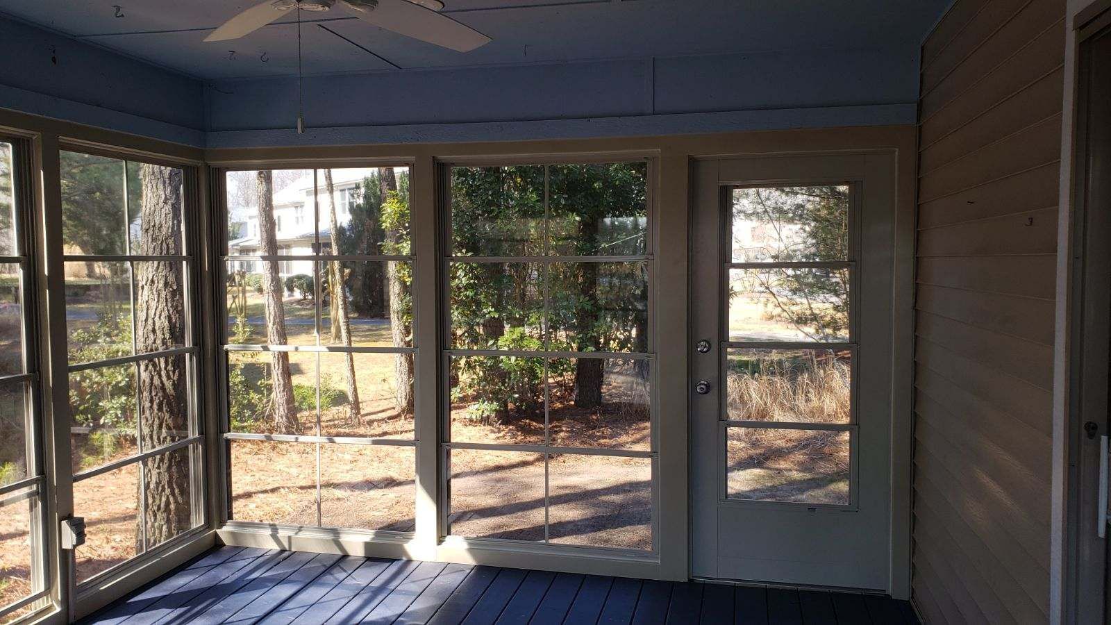A screened in porch with a lot of windows and a ceiling fan.
