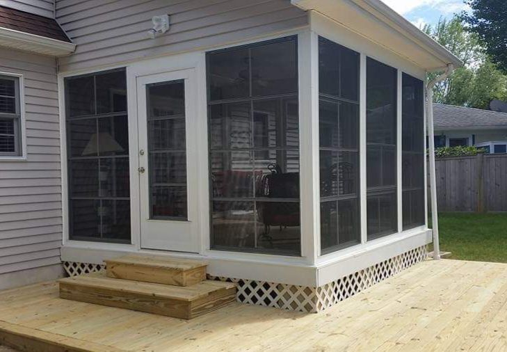 A screened in porch with a wooden deck in front of a house.
