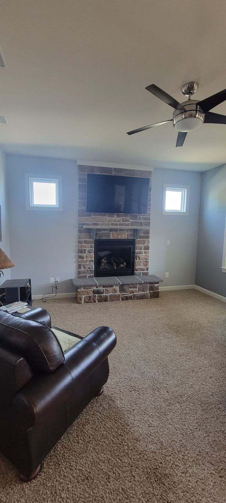A living room with a couch, chair, fireplace and ceiling fan.