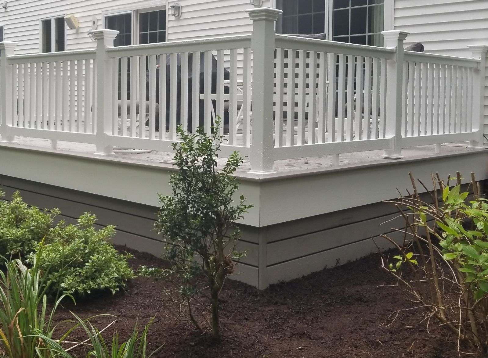 A white deck with a white railing and a white house in the background