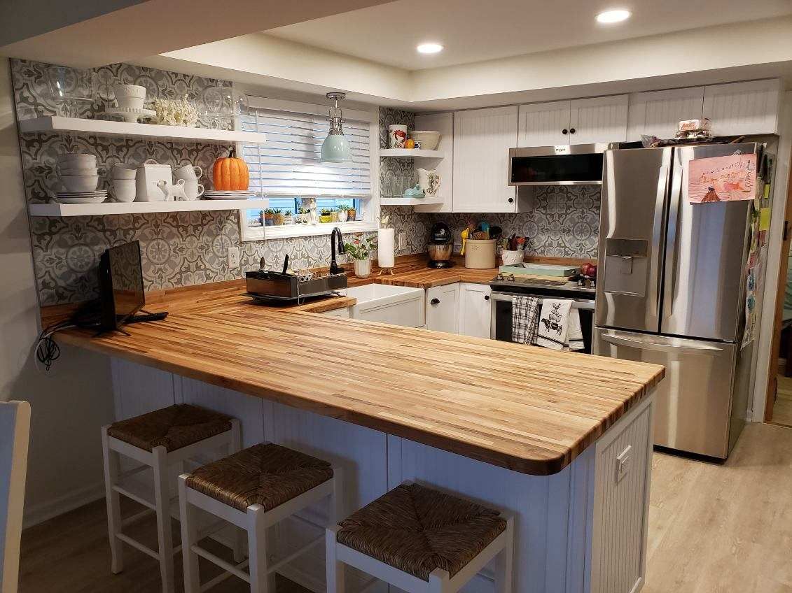 A kitchen with a wooden counter top, stools and a refrigerator.