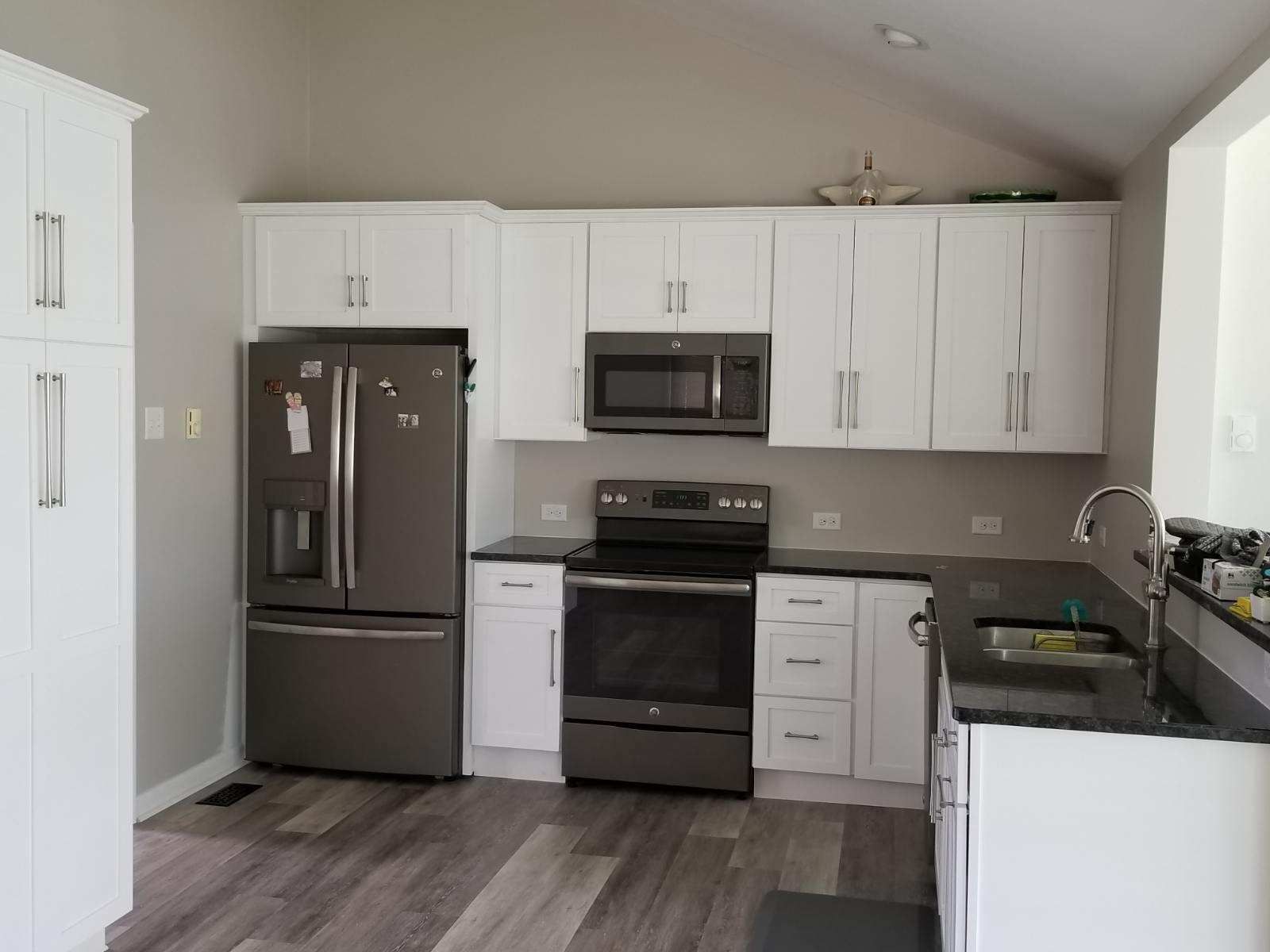 A kitchen with white cabinets, a refrigerator, stove, microwave and sink.