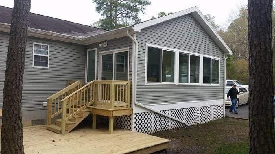 A man is standing in front of a house with a porch and stairs.