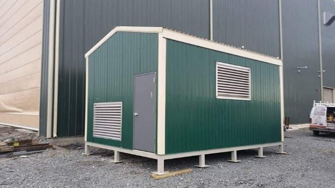 A small green shed is sitting in front of a building.
