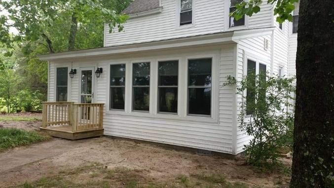 A white house with a large porch and lots of windows.