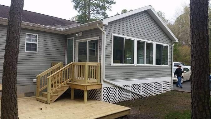 A man is standing in front of a house with a porch and stairs.
