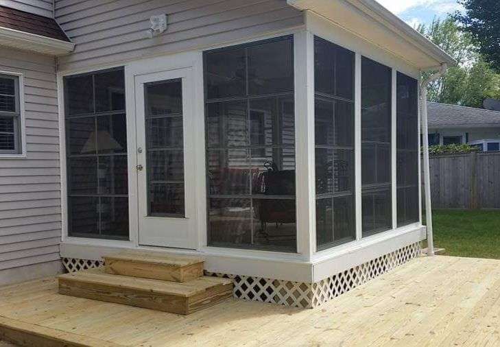 A screened in porch with a wooden deck in front of a house.
