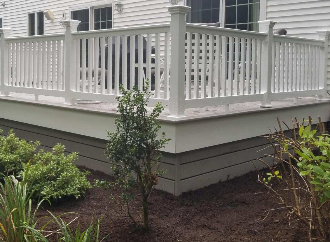 A white deck with a white railing and a white house in the background