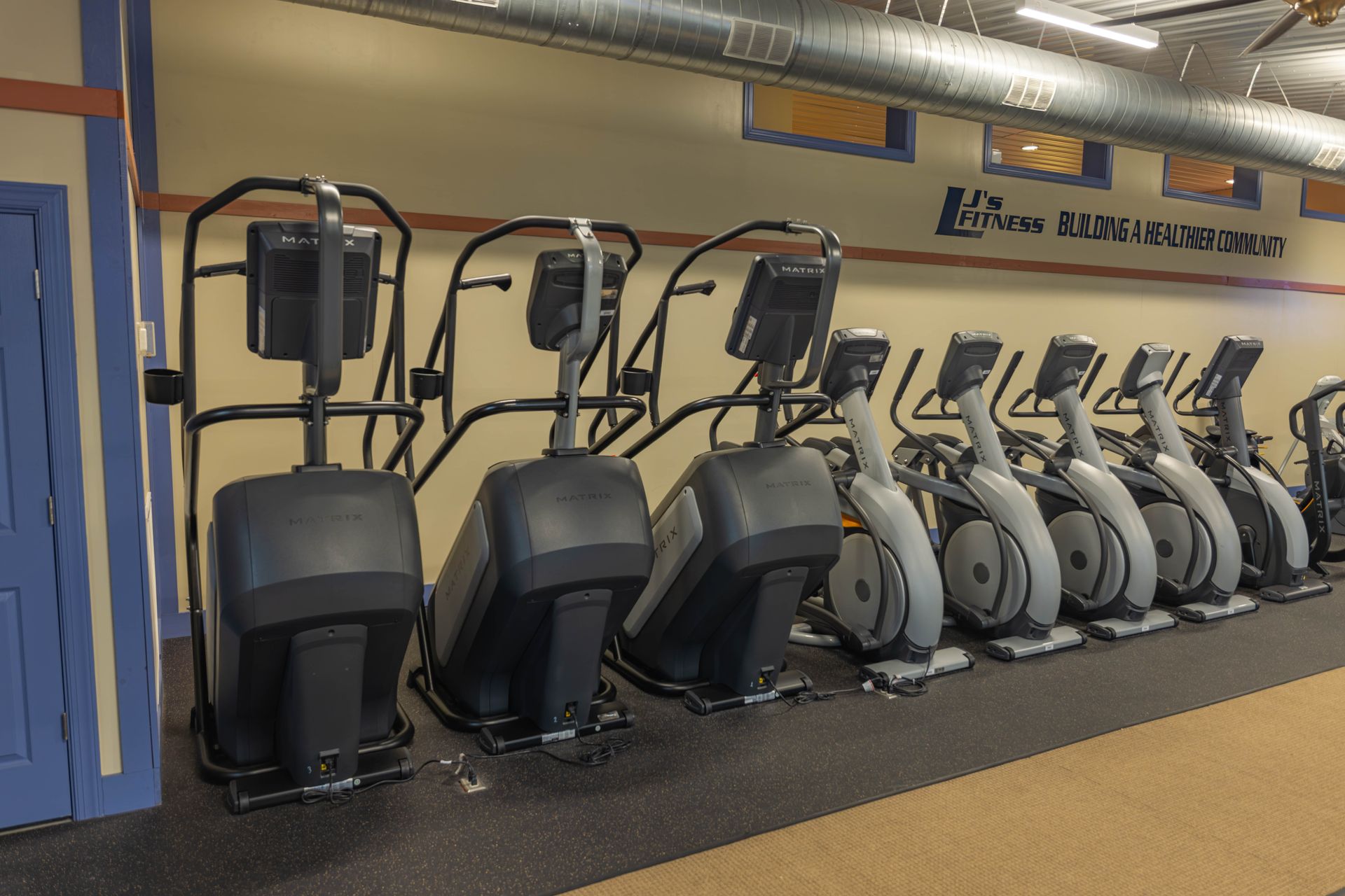 A row of grey elliptical machines lined up against a wall in a fitness center.