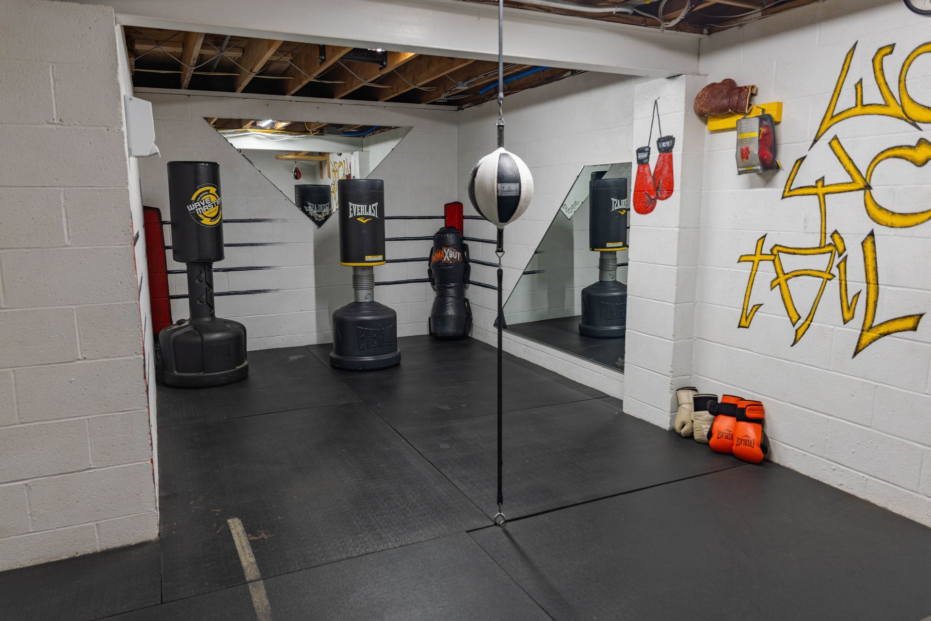 A home gym with three standing punching bags, a floor-to-ceiling speed bag, and boxing gloves on the floor.