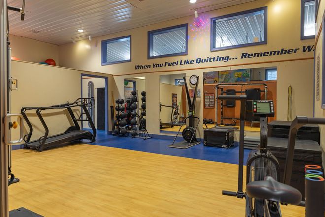 An empty gym with treadmills, a weight rack, and workout equipment on a light wood floor and blue exercise mat.