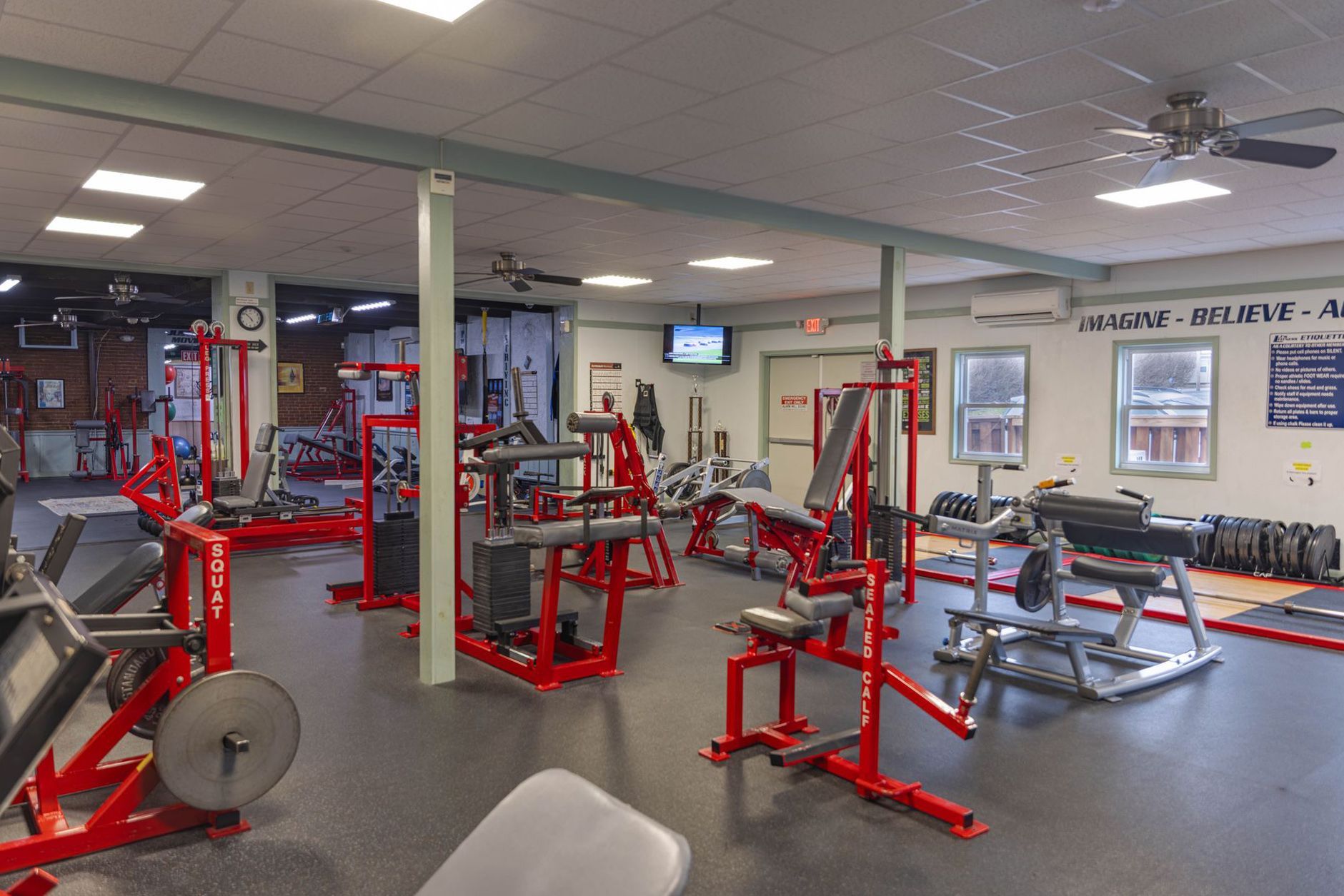 A gym interior with red weight machines on a gray floor, illuminated by overhead lighting.