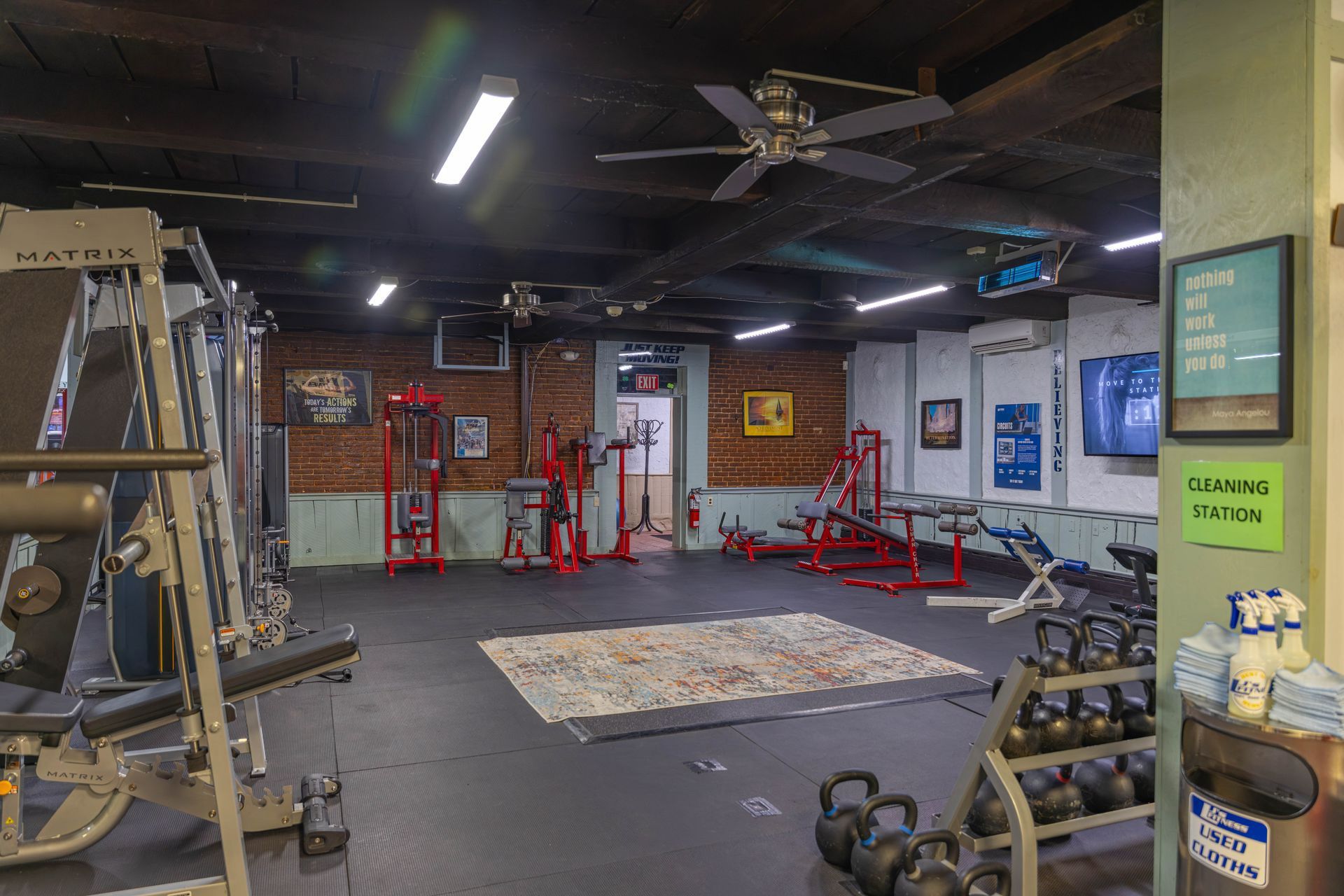 An industrial-style gym with exposed brick walls, strength training equipment, kettlebells, and an area rug.