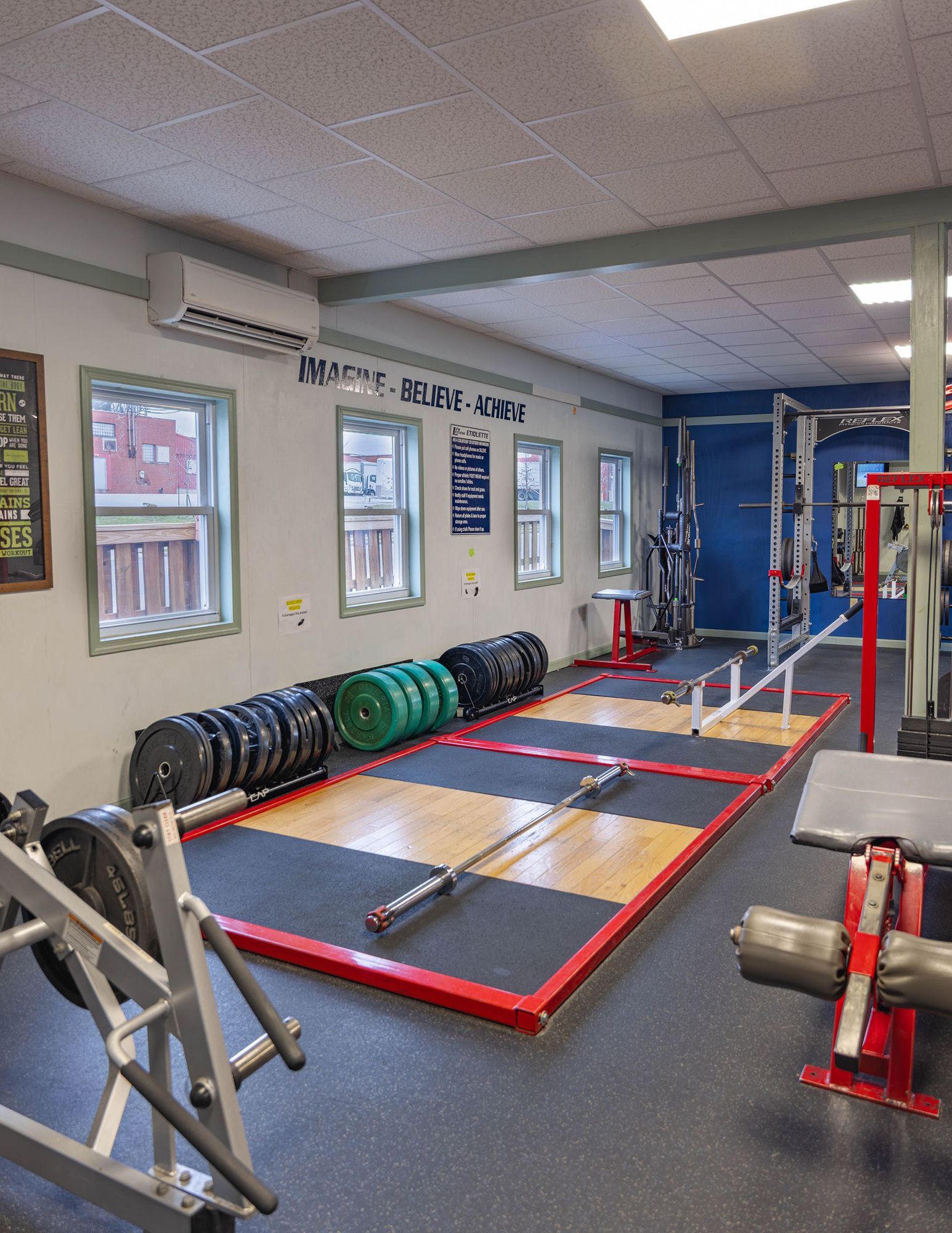 Weightlifting gym interior featuring multiple lifting platforms with barbells, weight plates, and various workout equipment.