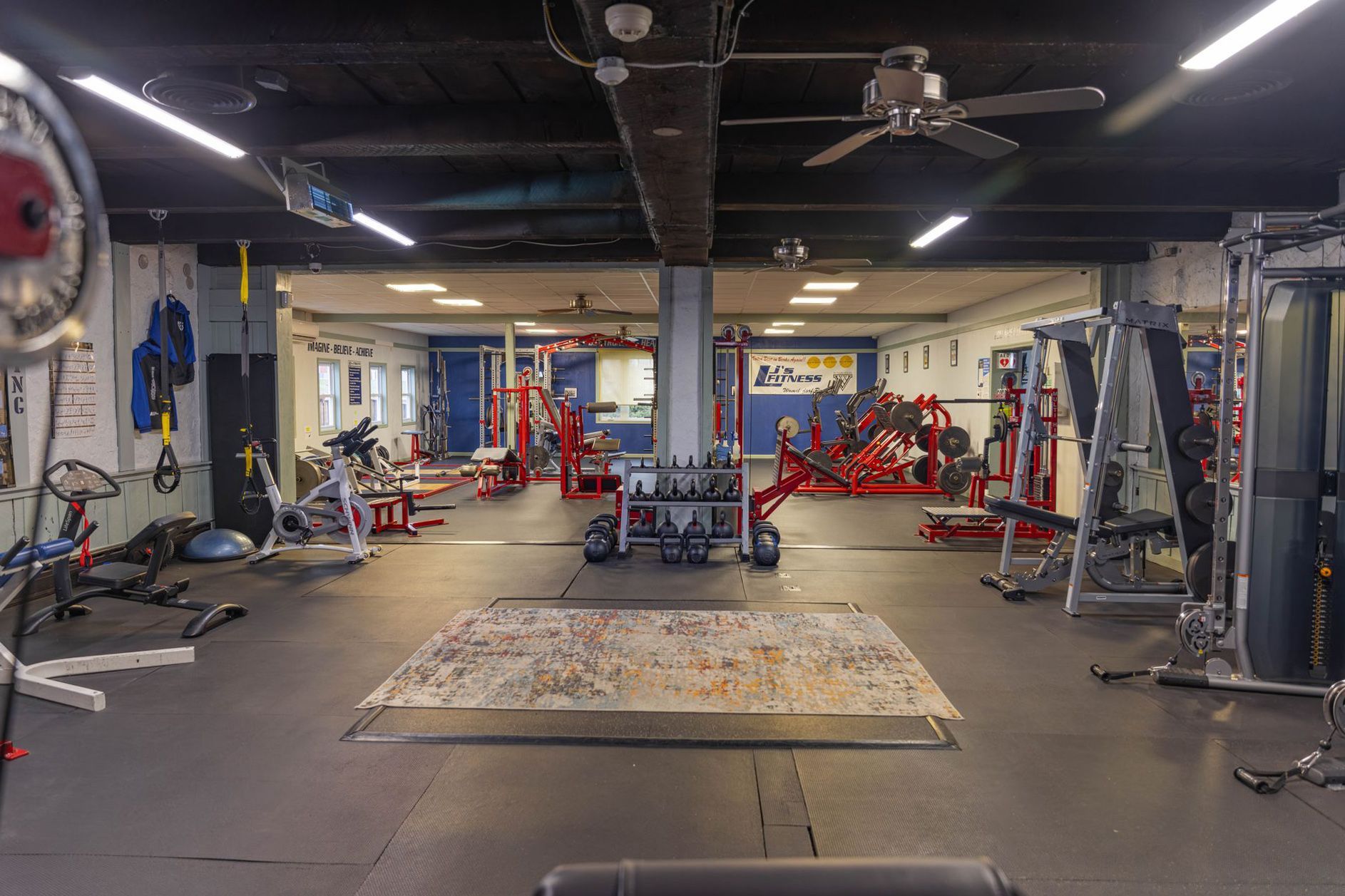 A spacious fitness center featuring weightlifting equipment, workout machines, and a large patterned rug in the center.