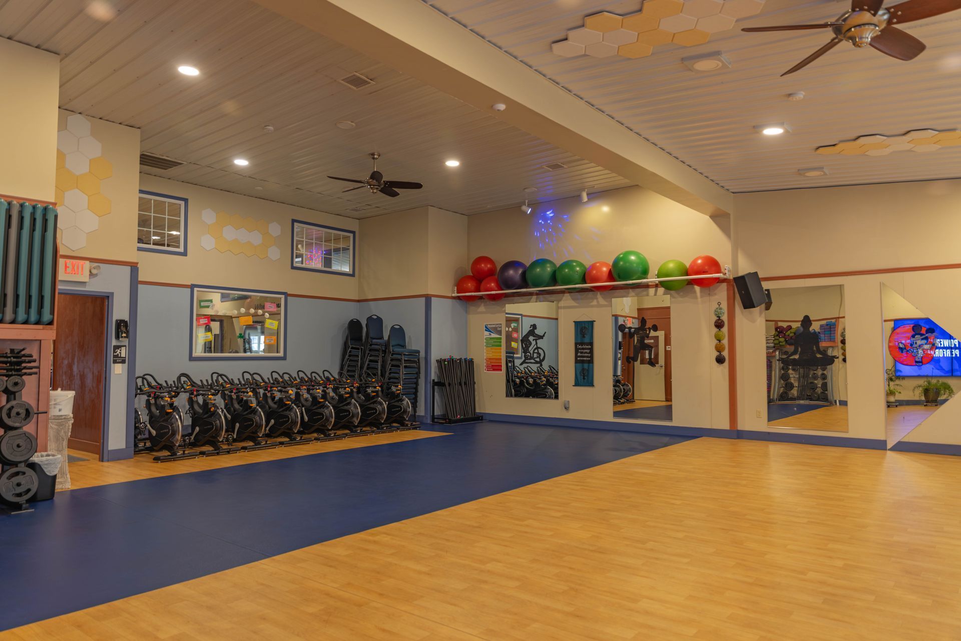 An indoor gym studio with a row of stationary bikes, mirrors on the wall, and exercise balls on a ledge.