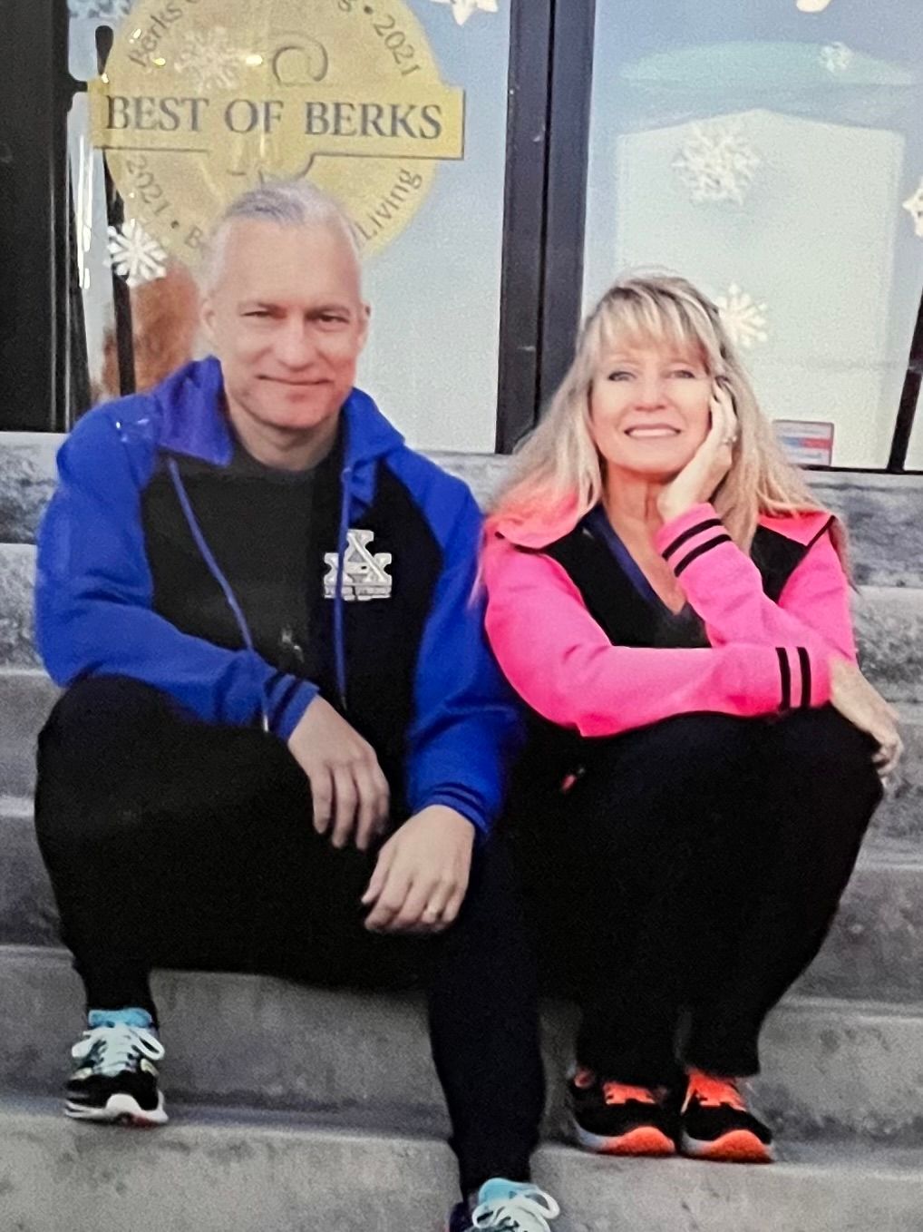 Two people sit on concrete steps in front of a glass door with a 