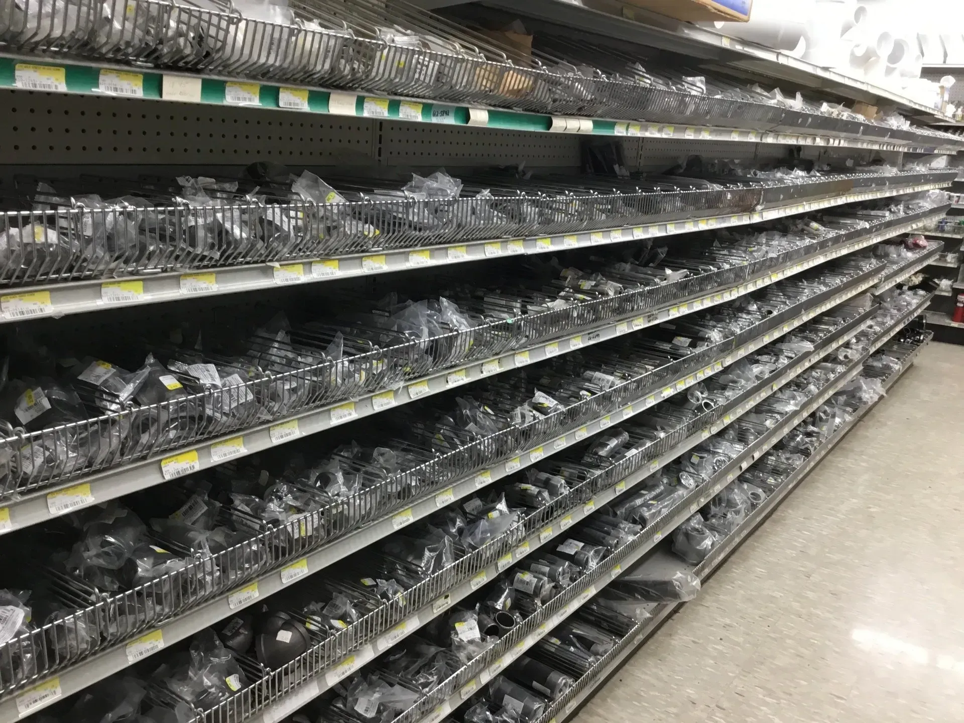 Empty store shelves lined with rows of small plastic trays in a brightly lit aisle