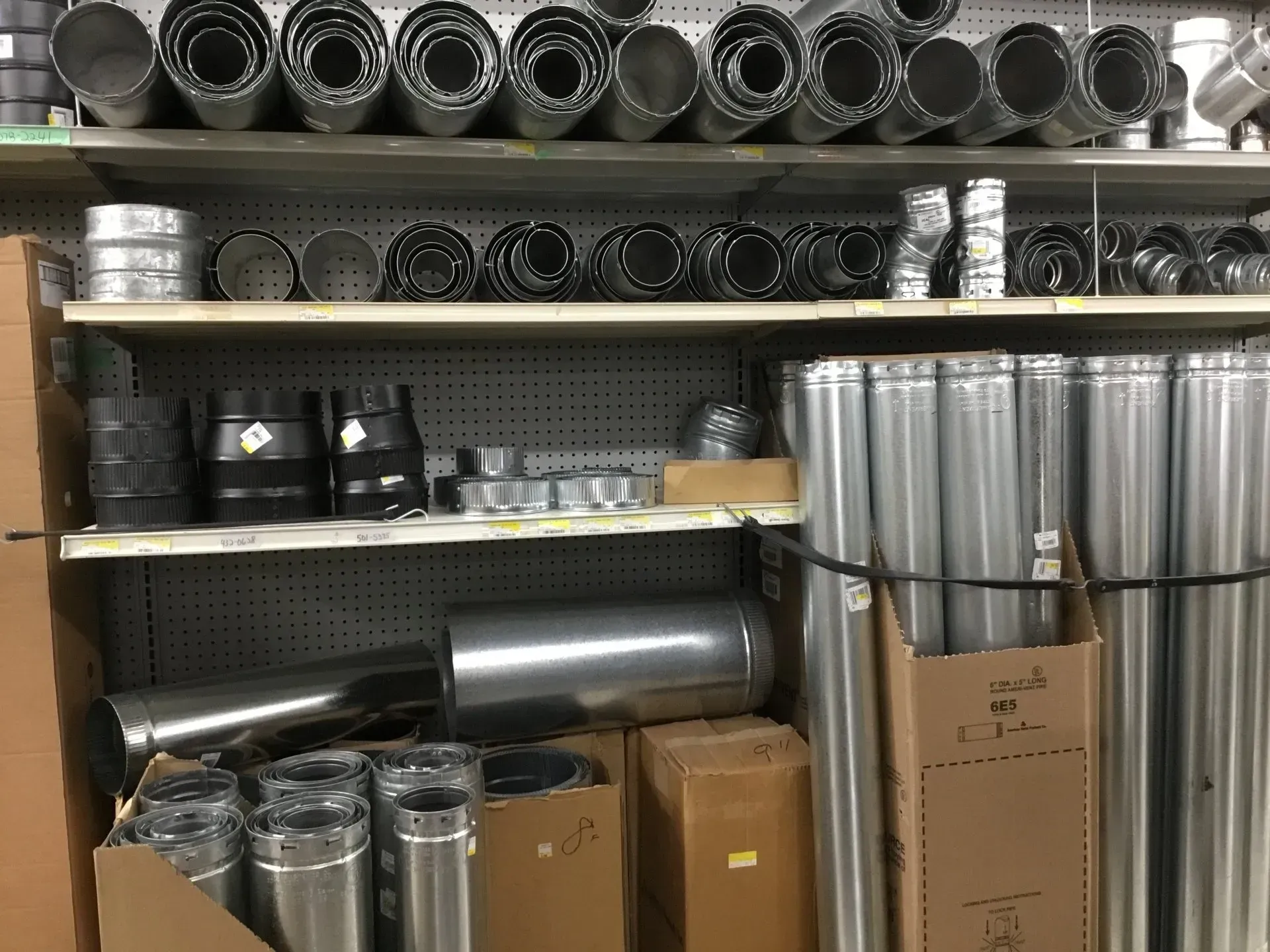 Shelves stocked with metal ducting, vent parts, and cardboard boxes in a warehouse.